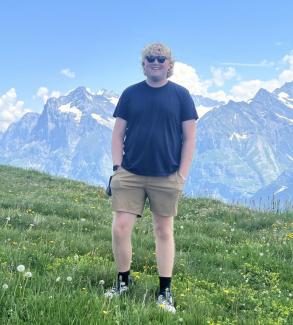 Charles Dew in Switzerland, photographed in front of the scenic Swiss Alps on a mountainside.