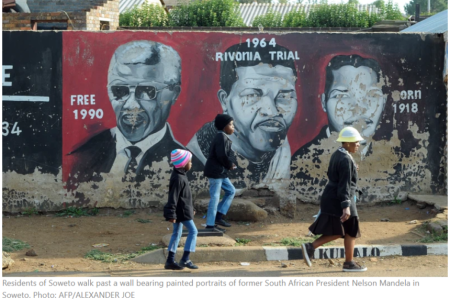 Residents of Soweto walk past a wall bearing painted portraits of former South African President Nelson Mandela in Soweto. Photo: AFP/ALEXANDER JOE 